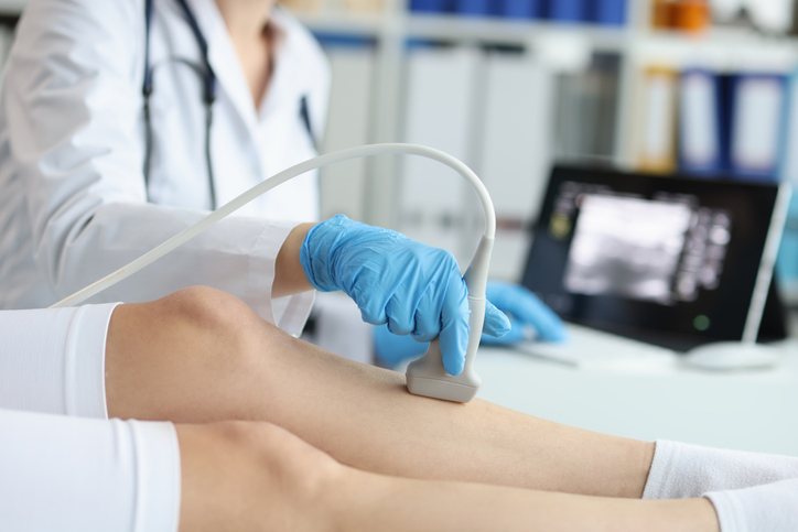 A sonographer scans a patient's legs with the images on the monitor