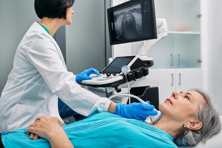 A sonographer performs a carotid ultrasound while the patient rests, the image on the monitor