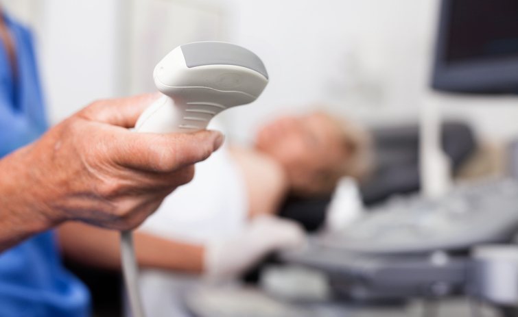A sonographer holds an ultrasound probe beside a patient at rest